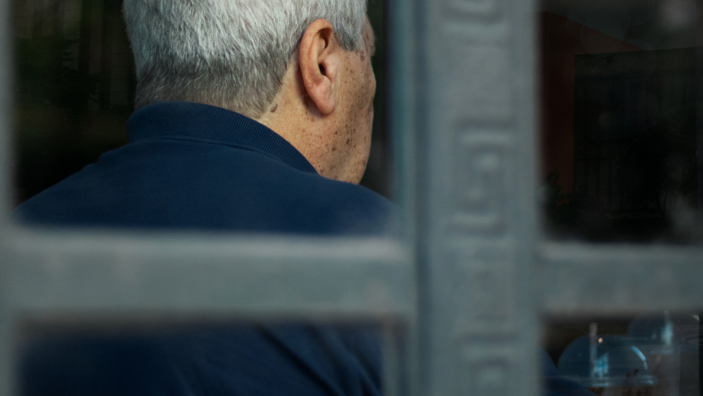 Photograph taken through a window of the back of a man's head who is sat at a table